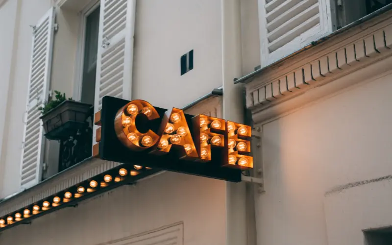 Illuminated cafe sign with vintage bulb lighting showing business identification signage on building exterior