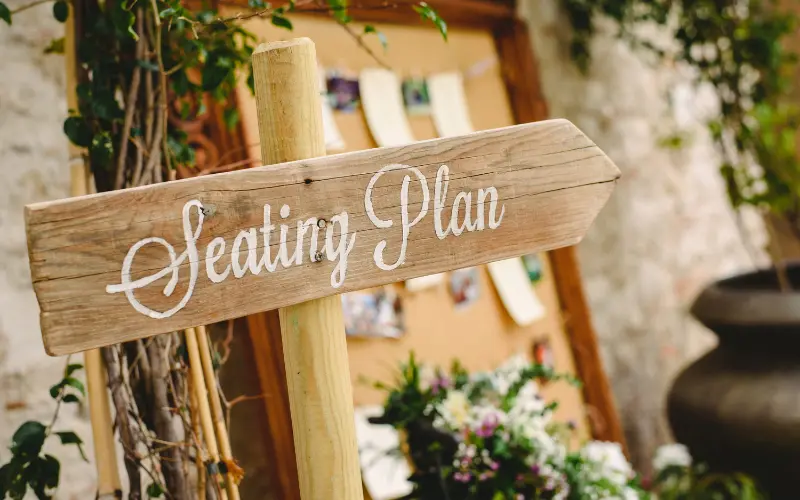 Wooden directional signboard displaying seating plan information at wedding venue entrance with rustic finish