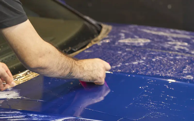 Do Car Wraps Damage Paintwork? The Truth About Vinyl Wrap Effects 2 Installer using a squeegee to apply vinyl wrap smoothly on a car bonnet, showing correct car wrapping methods for a clean finish.