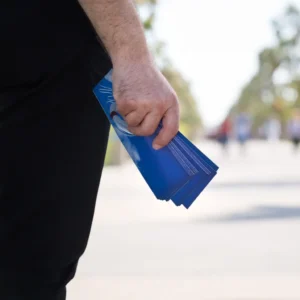 A person holding a stack of printed flyers and leaflets, showing promotional flyer distribution used for marketing events and local advertising.