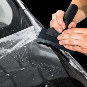 Applying vinyl car graphics using a squeegee to smooth vehicle wrap film during professional car graphics installation.